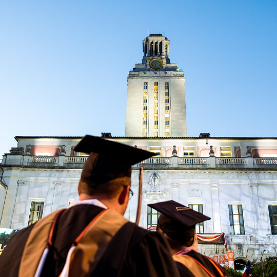 Graduate in commencement regalia looking up at University of Texas tower