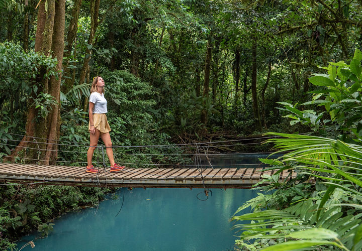 Person in rainforest walking on bridge over lagoon, Costa Rica