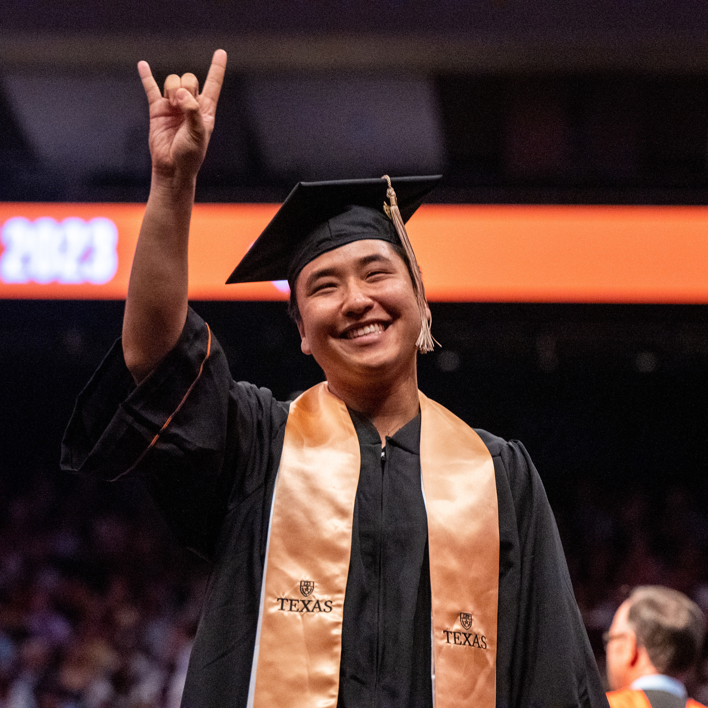 A student shows horns up as he walks across the graduation stage.