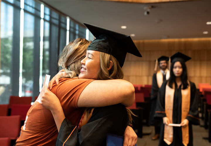Graduate in cap and gown hugs a family member