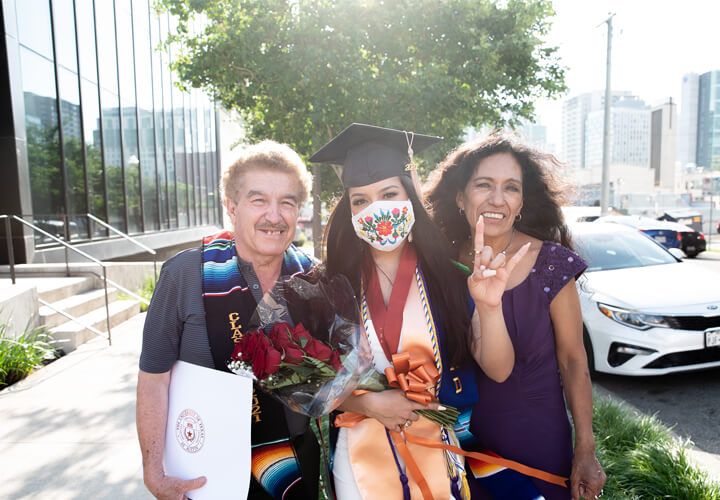 Masked graduate poses with family and gives hook em horns