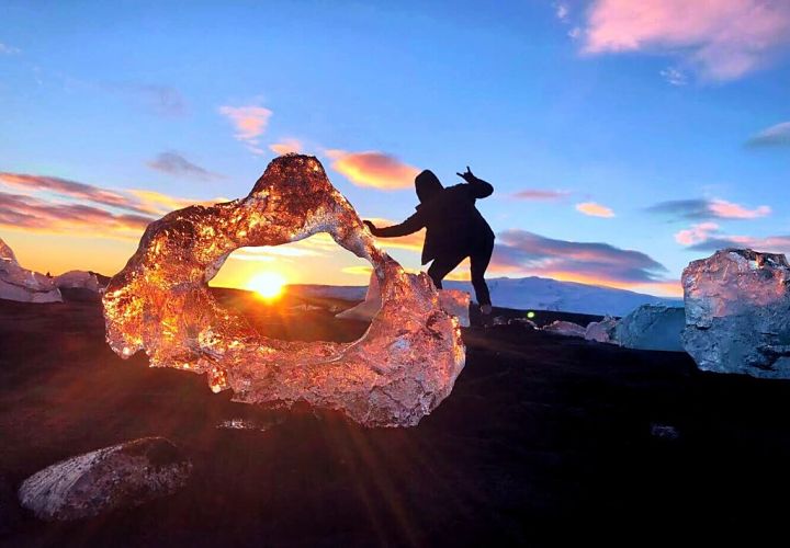 Person gives peace sign with sun shining through hole in ice sculpture